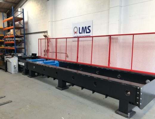 Black Horizontal tensile test machine with red guards open. Sign on the wall says LMS