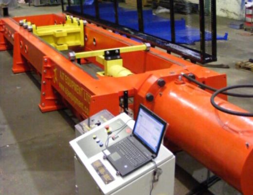 Orange horizontal tensile test machine with yellow ce=levis inside and black mesh guards- also shows electrical control cabinet with laptop open on top